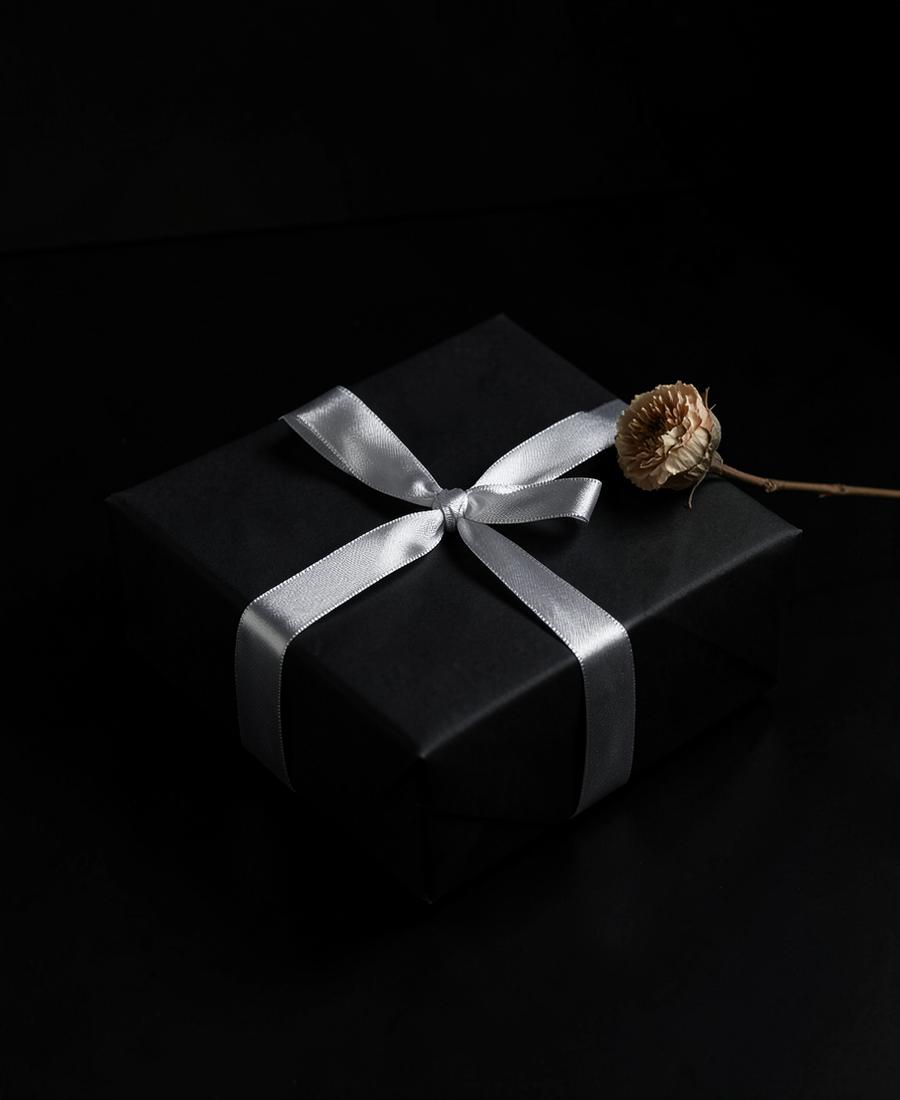 Black gift box tied with silver ribbon and a dried bloom